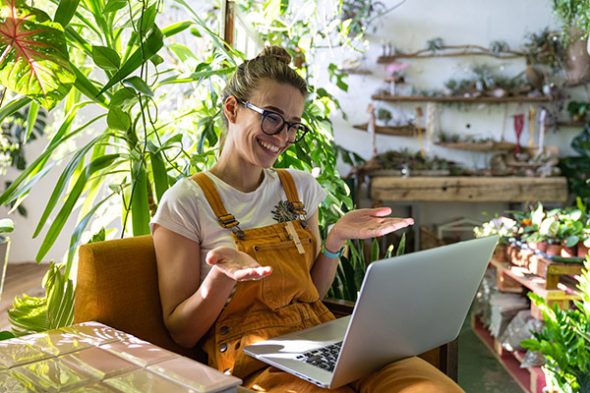 Woman gardener sitting on chair in green house, using laptop aft