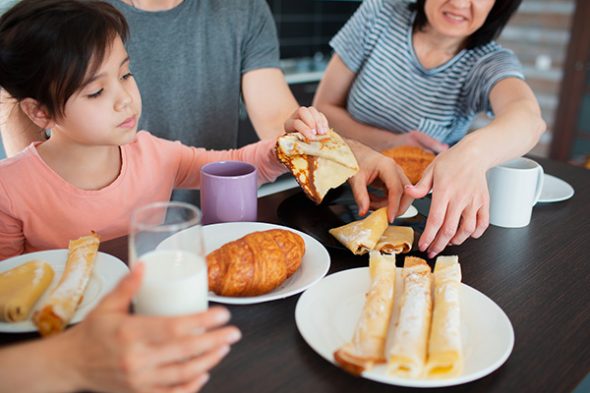 Close-up. Happy breakfast of a large family in the kitchen. Siblings, parents and children, mother and grandmother. Father and daughter. Everyone is eating in the morning and chatting and having fun.